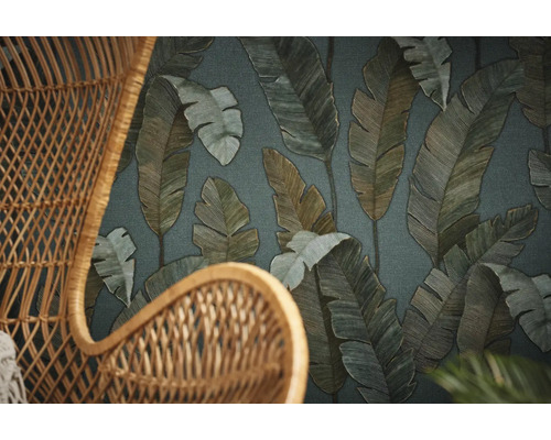 Gros plan d''un fauteuil en osier devant un papier peint à motifs de feuilles.