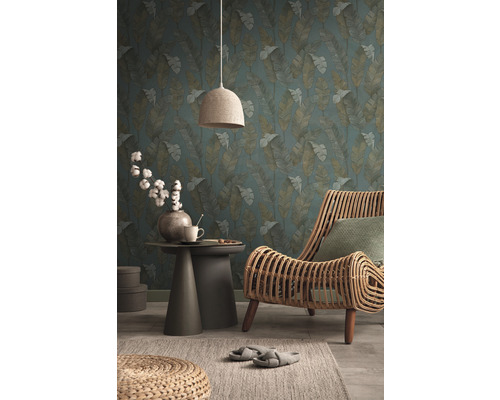 Salon avec papier peint à motif de feuilles, fauteuil en rotin, table d''appoint et lampe en textile pour une ambiance chaleureuse