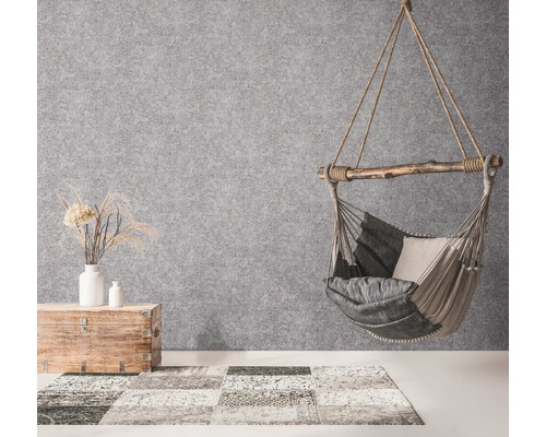 Fauteuil suspendu avec coussins, coffre en bois avec décoration et tapis dans une pièce lumineuse.