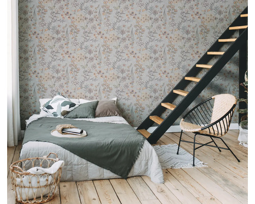 Chambre avec papier peint à motifs floraux, lit, échelle et fauteuil en rotin