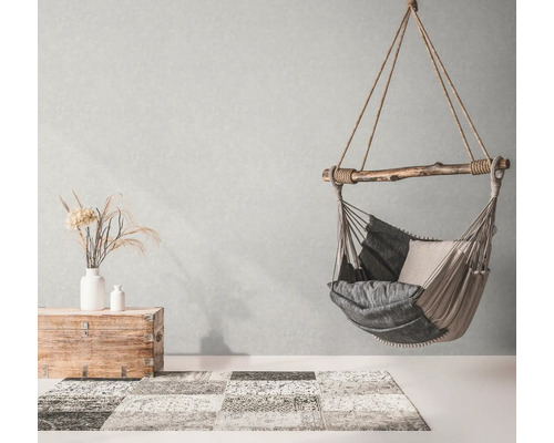 Fauteuil suspendu avec coussins, coffre et tapis dans une pièce lumineuse