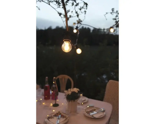 Festlich gedeckter Tisch im Freien mit Lichterkette für eine gemütliche Atmosphäre.