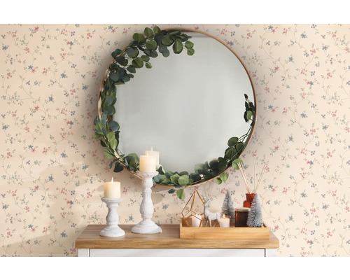 Miroir rond décoratif avec guirlande d''eucalyptus, bougies, cerf décoratif et mini sapins de Noël sur une table devant un papier peint à motifs floraux.