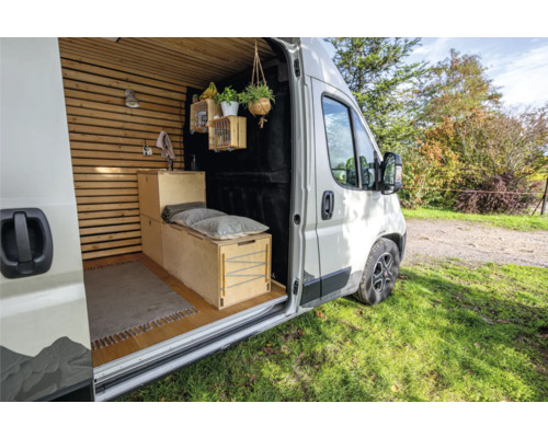 Innenansicht eines ausgebauten Kastenwagens mit Holzboden, Holzwandverkleidung, Bett und Dekoration