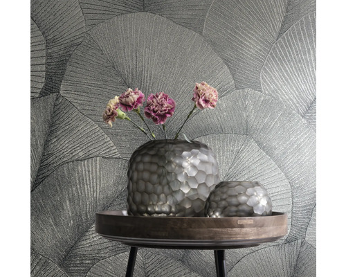 Deux vases et des fleurs sur une table devant un mur avec du papier peint à motifs de feuilles.