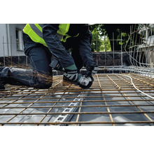 Ein Handwerker kniet auf einer Baustelle und schneidet mit einem Metabo Winkelschleifer Stahlträger, wobei Funken sprühen.