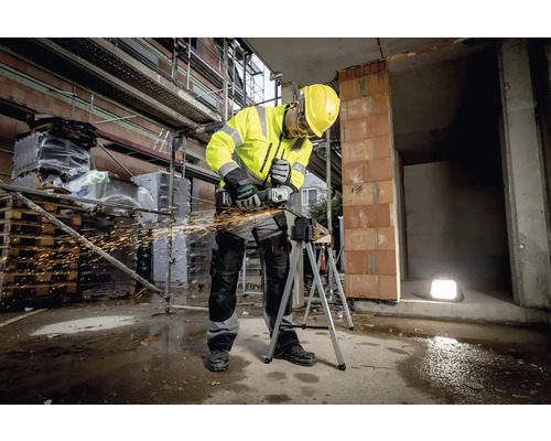 Ein Bauarbeiter in Arbeitskleidung benutzt einen Winkelschleifer auf einer Baustelle