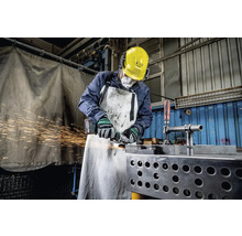Ein Arbeiter mit Schutzhelm, Gehörschutz, Atemschutzmaske und Schürze schleift Metall mit einem Winkelschleifer, wobei Funken sprühen.