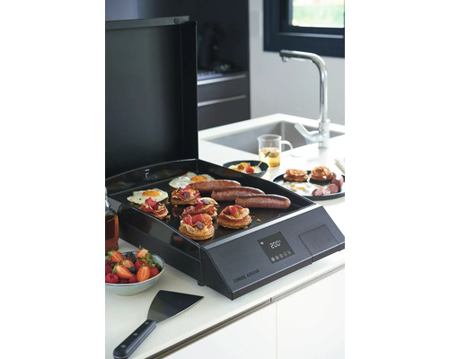 Plancha électrique avec des aliments tels que des œufs, des saucisses et des pâtisseries dans une cuisine.