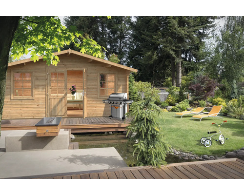 Abri de jardin Palmako Klara 17,0 m² 518 x 420 cm apprêté par immersion marron Scène avec une cabane de jardin en bois, un barbecue, des chaises longues et un tricycle pour enfants dans un jardin.