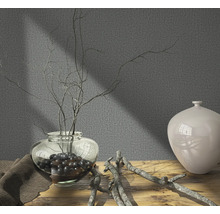 Scène décorative avec vase, branches et tissu textile sur table en bois devant un mur gris