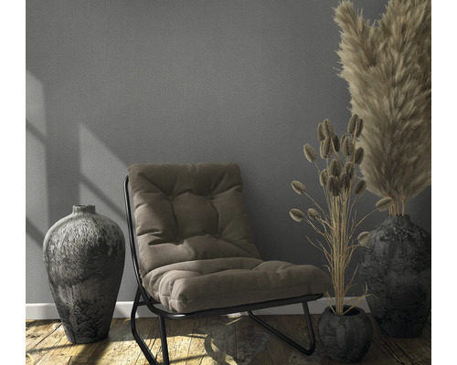 Einrichtungsszene mit Sessel, Vasen und Trockenblumen auf Holzboden vor einer Wand.