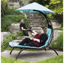 Scène d''extérieur avec chaise longue suspendue, une personne est allongée sur la chaise longue avec un magazine, une autre personne est assise sur un escalier