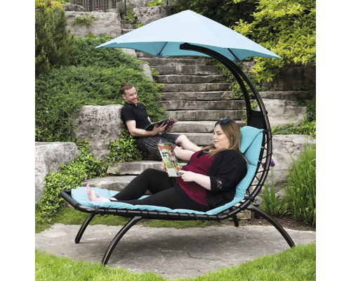 Scène d''extérieur avec chaise longue suspendue, une personne est allongée sur la chaise longue avec un magazine, une autre personne est assise sur un escalier