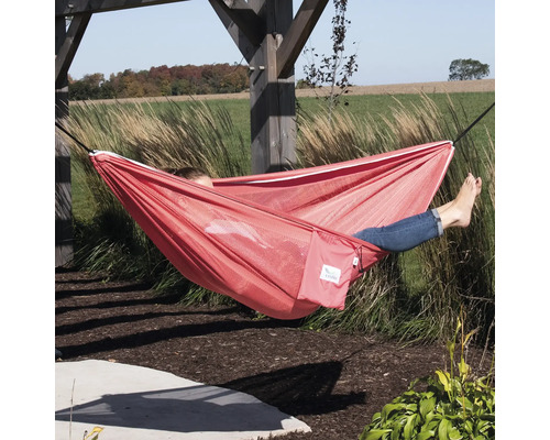 Person liegt in einer roten Hängematte im Garten.