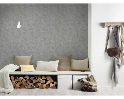 Wohnraumszene mit grauer Strukturtapete, Sitzbank mit Kissen und Holzscheiten