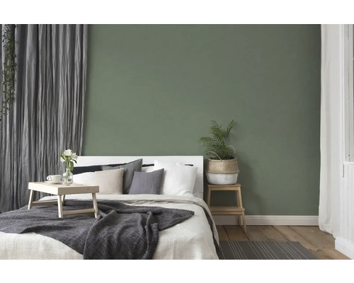 Schlafzimmer mit Bett, Nachttisch und Dekoration vor einer grünen Wand