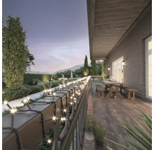 Terrasse avec guirlande lumineuse sur une rambarde avec jardin en arrière-plan.