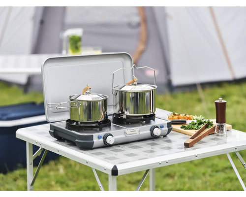 Réchaud de camping avec deux casseroles sur une table avec des aliments devant une tente