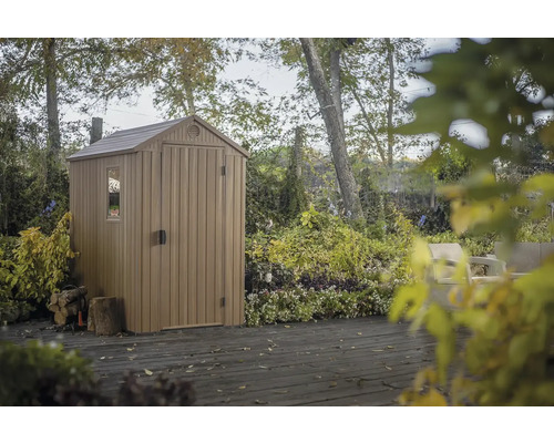 Gartenhaus aus Kunststoff mit Fenster und Tür auf einer Holzterrasse, umgeben von Bäumen und Pflanzen.