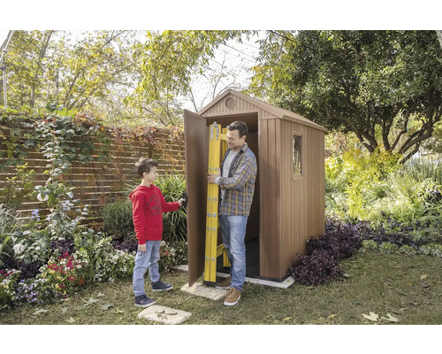 Ein Mann und ein Junge vor einem Gartenhaus mit geöffneter Tür, in der eine Leiter steht.