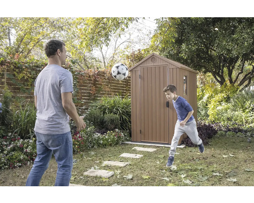 Vater und Sohn spielen mit einem Fußball vor einem Gartenschuppen im Garten.