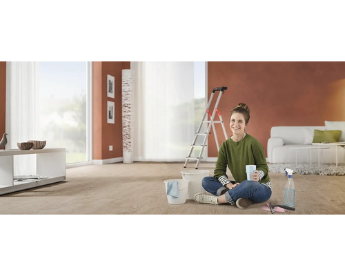 Femme assise par terre avec un seau et des produits de nettoyage dans le salon