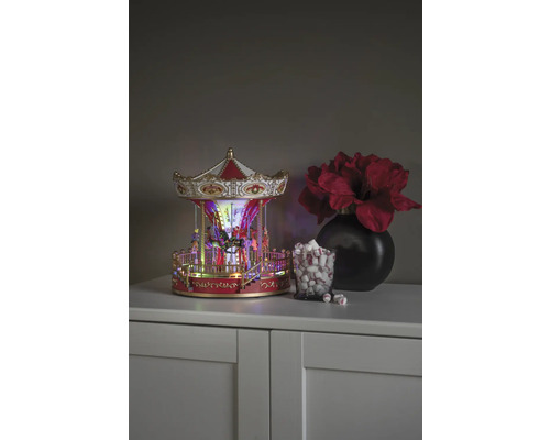 Dekoratives Karussell mit Beleuchtung, neben einem Glas mit Marshmallows und einer Vase mit Blumen auf einem Schrank