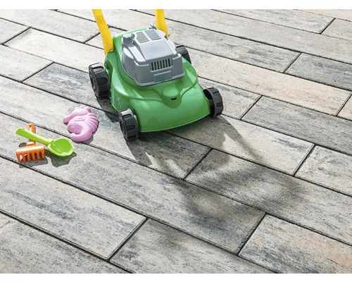 Spielzeugrasenmäher und Sandspielzeug auf Pflastersteinen