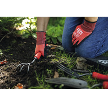 Gartenszene mit Person, die Gartenhandschuhe trägt und eine Gartenkralle im Boden verwendet.