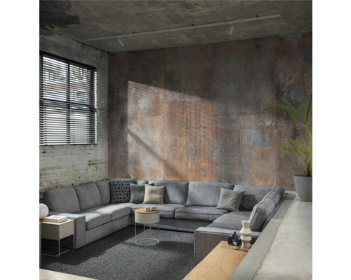 Canapé d''angle gris avec coussins et tables d''appoint dans un espace de vie industriel avec des murs en béton et une fenêtre avec des stores.
