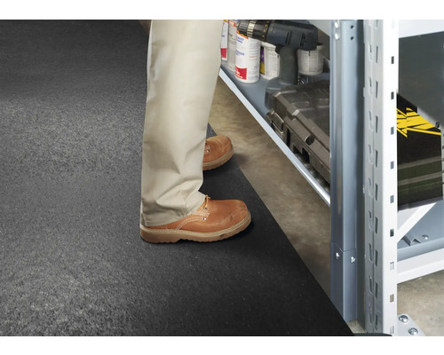 Un homme se tient sur un tapis de caoutchouc devant une étagère de stockage avec des outils et des accessoires.