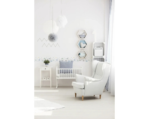 Hell gestaltetes Kinderzimmer mit Babybett, Sessel und dekorativen Elementen.
