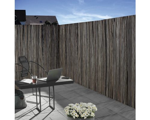 Sichtschutzzaun aus Naturmaterial neben einem Gartentisch mit Laptop im Aussenbereich.