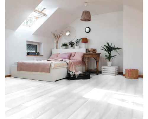 Chambre mansardée avec parquet en bois blanc, lit et fenêtre de toit.