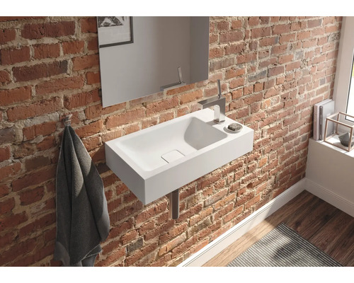 Salle de bains avec lavabo blanc sur un mur de briques, complété par un miroir et des robinets.