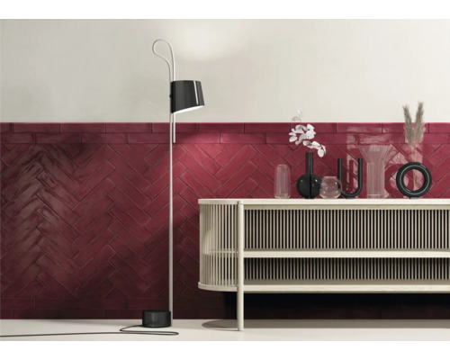 Décoration murale avec des carreaux rouges en motif à chevrons, combinée avec un lampadaire moderne et un buffet.