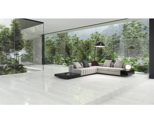 Espace de vie lumineux avec canapé d''angle, lampadaire et vue sur une végétation luxuriante à travers une grande paroi vitrée.