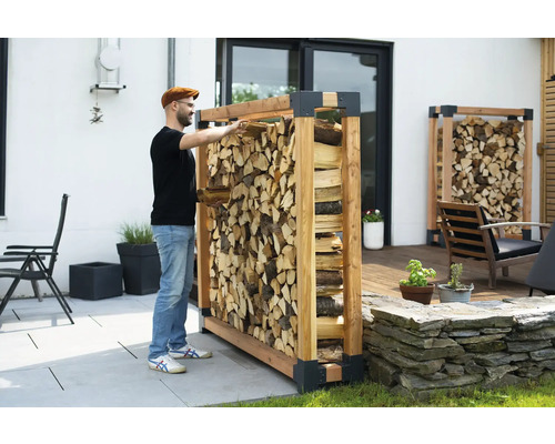 Un homme range du bois de chauffage dans un étagère à bois dans le jardin.