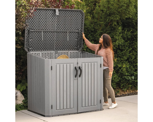 Armoire de jardin grise avec couvercle et portes ouverts devant une femme dans le jardin