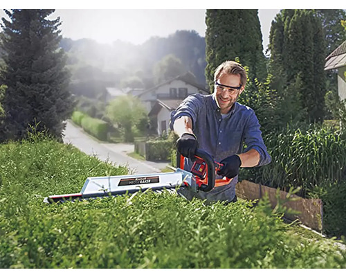 Un homme taille une haie avec un taille-haie à l''extérieur.