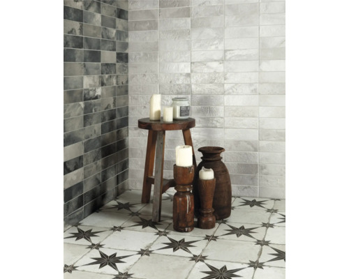 Badezimmer mit grauen und weissen Wandfliesen und Bodenfliesen mit Sternmuster, dekoriert mit Kerzen und Holzhockern.