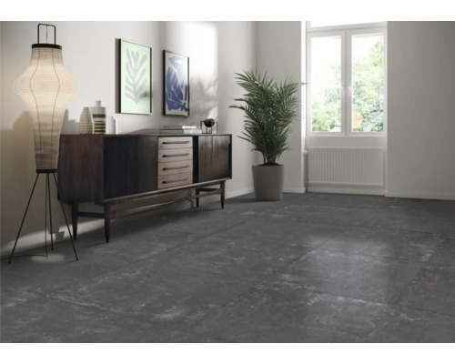 Wohnraum mit dunklen Bodenfliesen, Kommode, Stehlampe und Zimmerpflanze