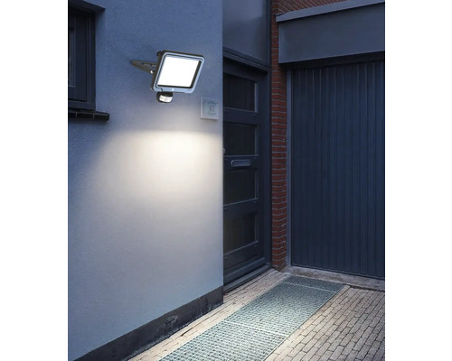 Aussenaufnahme einer beleuchteten LED-Aussenleuchte mit Bewegungsmelder an einer Hauswand