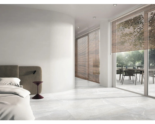 Helles Schlafzimmer mit Fliesenboden, Jalousien und Zugang zu einer Terrasse mit Gartentisch und Stühlen.