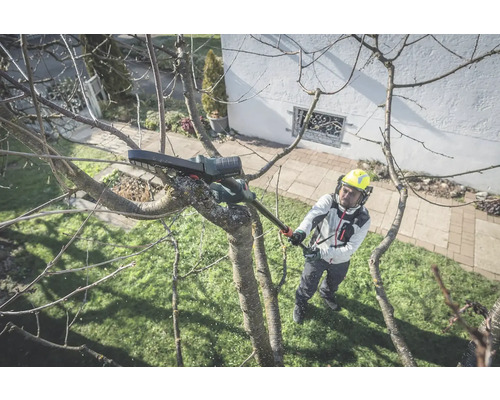 Un homme portant un casque et des protections auditives coupe des branches avec une tronçonneuse à manche.