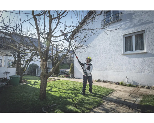 Une personne portant un casque de sécurité utilise un ébrancheur pour tailler un arbre dans le jardin.
