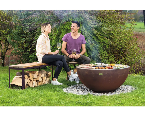 Personen sitzen auf einer Bank neben einem Kugelgrill im Garten