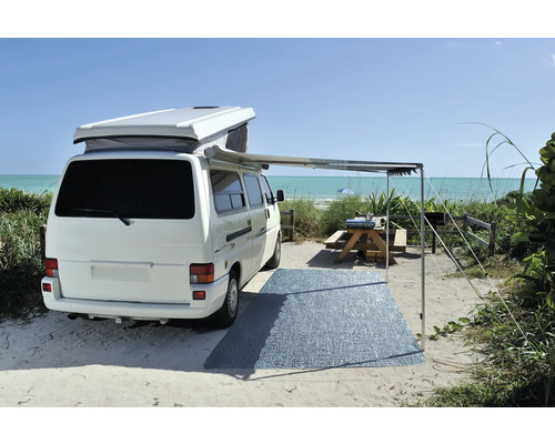 Weisser Campingbus mit Markise und Picknickplatz am Strand.