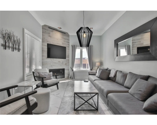 Wohnzimmer mit Sofa, Sessel, Fernseher und Kamin.